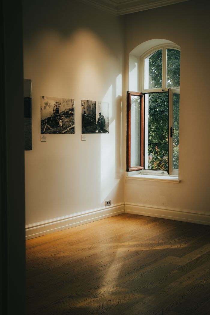 services-01 Art gallery corner with sunlight through an open window, highlighting framed photographs on a white wall.