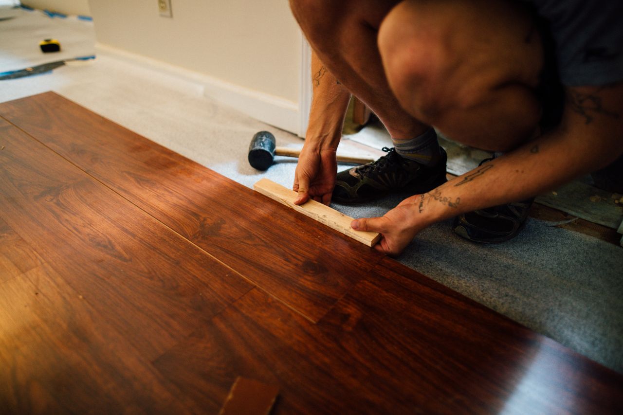 hero-02 Faceless male master laying wooden laminate flooring using mallet in apartment during renovation
